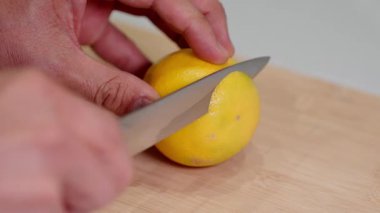 Kişinin detaylı yakın plan çekimi olgun bir limonu ahşap kesme tahtasındaki bıçakla ustalıkla dilimler. Taze malzemeler, sağlıklı yemekler, narenciye tarifleri, detoks içecekleri gibi konular için idealdir.