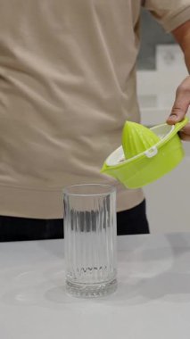 Taze limon suyunu elle tutulan el sıkma makinesinden dikey şarjörle şeffaf bardağa dök. Mobil mutfak düzenlemesi, sağlıklı içecek hazırlığı, narenciye içeceği konsepti.