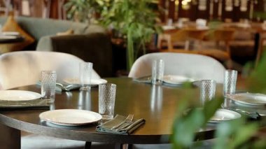 Bişkek, Kırgızistan - 22 Ocak 2026: Tabaklar, bardaklar, çatal bıçaklar ve peçetelerle dolu lüks restoran masası. Sıcak ışık, yeşillik ve yumuşak arka plan bulanıklığıyla samimi modern yemek içleri.