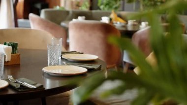 Bishkek, Kırgızistan - 22 Ocak 2026: Tabaklar, bardaklar ve çatal bıçaklarla akşam yemeği için boş restoran masası. Yumuşak ışık ve yeşillikle dolu, samimi, modern bir kafe. Misafirperverlik, yemek, yemek servisi.