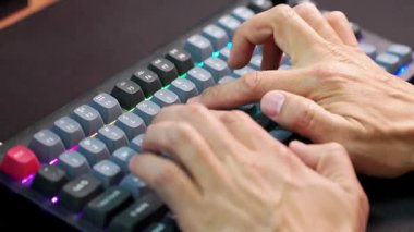 Işıklandırılmış mekanik klavyede RGB arka ışığı olan ellerin yakın çekimi. Programlama, oyun, uzaktan çalışma, dijital üretkenlik ve modern teknoloji çalışma alanı kavramı.