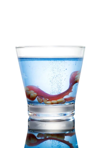 Limpieza de una dentadura postiza en un vaso con agua azul. . — Foto de Stock