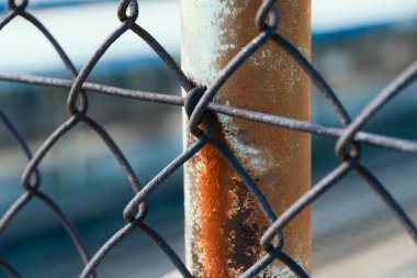 Paslı metal bir direğe bağlı eskimiş bir tel örgüye yakın plan.