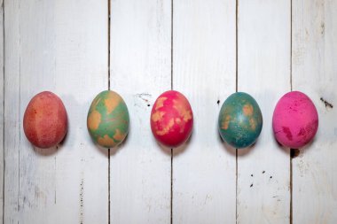 Paskalya yumurtalarını süslemek için ev yapımı doğal bir yöntem. Beş haşlanmış yumurta renklerle boyanmış, yapraklar ve çiçekler eski püskü ahşap bir masa üzerinde.. 