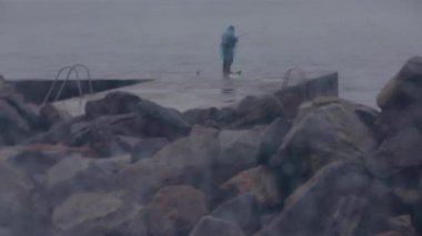 Yalnız balıkçı yağmurlu havalarda taş bir iskelede balık yakalar