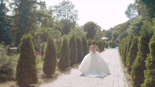 Die Braut in einem wunderschönen weißen prachtvollen Kleid läuft weiter, ist im Sommer mehr scharlachrot zwischen grünen Büschen, Zeitlupe — Stockvideo