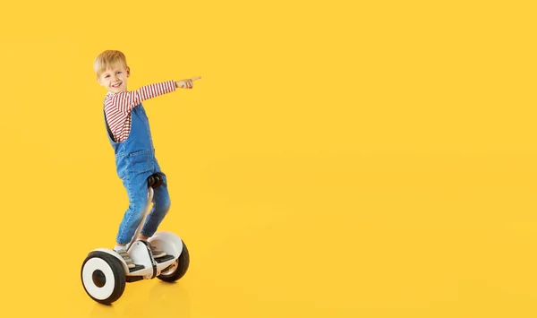 有趣的小男孩骑在悬浮板上或黄色背景的陀螺摩托车上 为儿童做广告的电动交通工具 — 图库照片