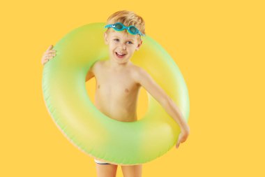 Yüzme gözlüklü, neon şişme lastik çemberli mutlu çocuk portresi sarı arka planda izole edilmiş eğleniyor. Yaz tatili 6 komik surat