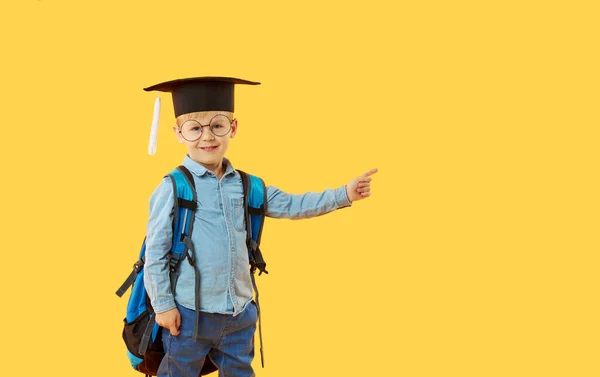 Student Základní Školy Čepicí Brýlemi Batohem Žlutém Pozadí Ukazující Rukou — Stock fotografie