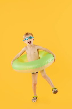 Yüzme gözlüklü, neon şişme lastik çemberli mutlu çocuk portresi sarı arka planda izole edilmiş eğleniyor. Yaz tatili 6 komik surat