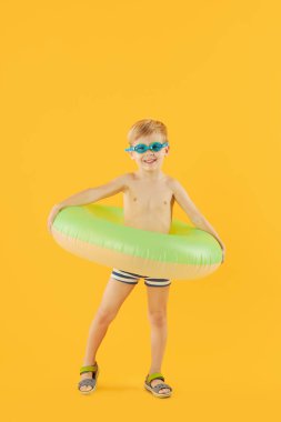 Yüzme gözlüklü, neon şişme lastik çemberli mutlu çocuk portresi sarı arka planda izole edilmiş eğleniyor. Yaz tatili 6 komik surat