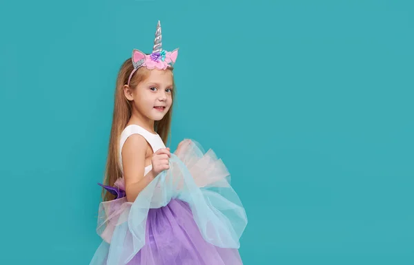 Unicorn girl. Funny face. Cute child girl in elegant tulle dress and unicorn headband celebrates birthday  party on colored background