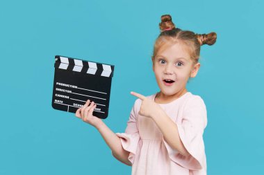 Funny smiling child girl hold film making clapperboard isolated on blue background. Little clipmaker, acting training. Funny face. Copy space for text.	