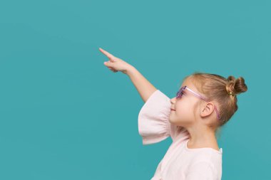 Mavi arka planda güzel güneş gözlüklü gülümseyen kız çocuğu portresi. Komik surat. Çocuklarda sağlıklı görme kavramı. Sola dönük.  