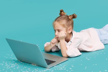 Cyan arka planında dizüstü bilgisayar kullanan akıllı kız. Eğitim, online çalışma, televizyon, uzaktan öğrenme. Karantina sırasında ilkokul öğrencisiymiş. Bilgisayardaki çocuklar için eğitici oyunlar