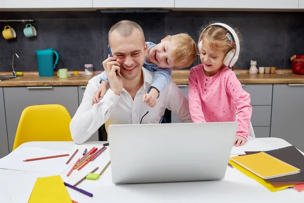 Father working from home during lockdown quarantine and closed school. coronavirus outbreak. Young businessman freelancer works on laptop with children playing around.