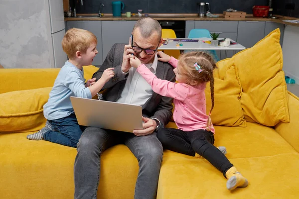 Father working from home with kids during quarantine lockdown and closed school. coronavirus outbreak. Young businessman freelancer works on laptop with children playing around.