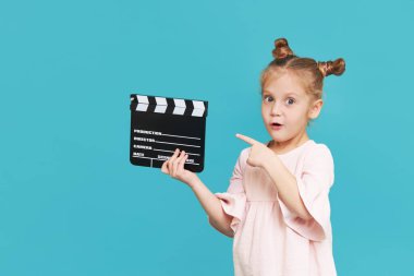 Funny smiling child girl hold film making clapperboard isolated on blue background. Little clipmaker, acting training. Funny face. Copy space for text.	