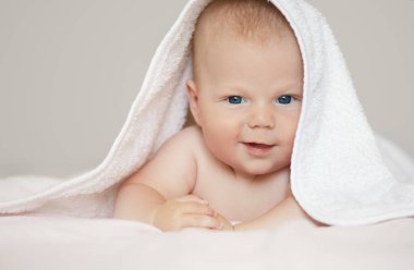 Beyaz arka planda beyaz havlu giymiş şirin bir çocuğun yakın plan portresi. Banyo yapan bebekler ve huzurlu bir uyku. Komik çocuk yüzü