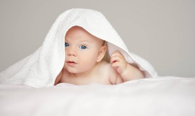 Beyaz arka planda beyaz havlu giymiş şirin bir çocuğun yakın plan portresi. Banyo yapan bebekler ve huzurlu bir uyku. Komik çocuk yüzü