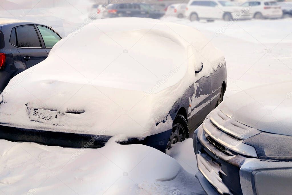 A snow storm covers cars with snow in an open parking lot.