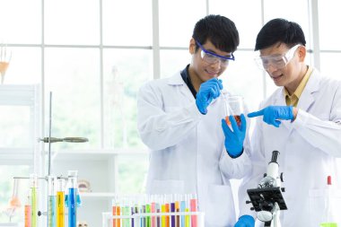 Güvenlik gözlüğü takan neşeli mikrobiyologlar test tüplerine gururla bakarken aynı zamanda yeni virüs aşısının üretimi ya da korunması üzerine çalışıyorlar..