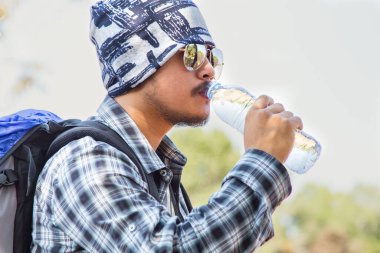 Genç bir Asyalı yürüyüşçü ya da ormanda sırt çantalı bir turist içme suyu içiyor..