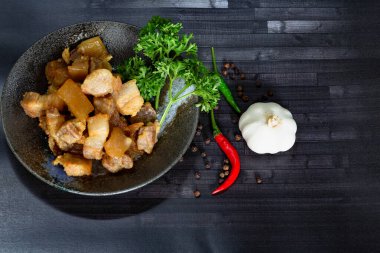 Öğle yemeği için siyah ahşap masada balık soslu, sarımsaklı, biberli ve siyah peperli kızarmış domuz eti..  