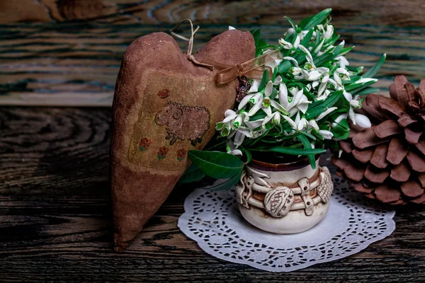 Die ersten Schneeglöckchen in Vase und Tannenzapfen. Herz. Holzstruktur — Stockfoto