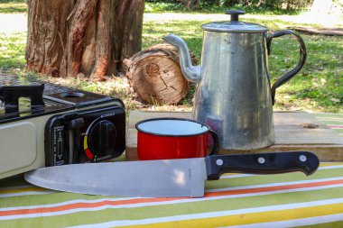 Kamp ve piknik seti gaz sobası, su ısıtıcısı kırmızı bardak el altında radyo ve masa örtüsü ve çimlerde ip. Açık hava yaşam ekipmanları.