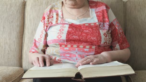 Anciana leyendo el libro en el sofá — Vídeos de Stock