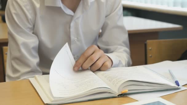 Student jongen achter een bureau te kijken naar het leerboek — Stockvideo