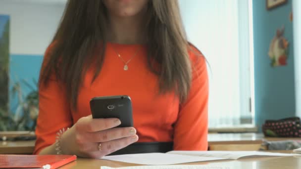 Menina jovem senta-se em uma mesa e mantém um telefone inteligente — Vídeo de Stock