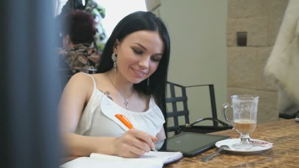 Snygg ung tjej skriver i dagboken i caféet — Stockvideo