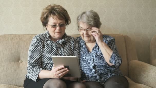 Две пожилые женщины смотрят фотографии с помощью планшета — стоковое видео
