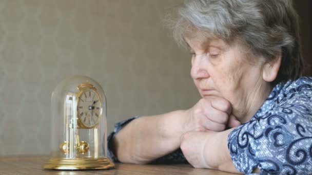 Oude vrouw kijkt naar de tafel klok met slinger — Stockvideo