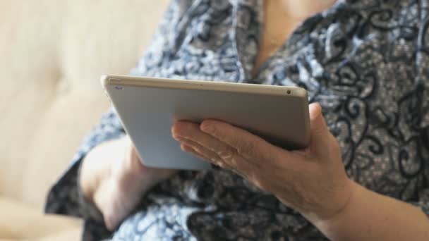 Old woman holding a digital tablet sitting on sofa — Stock Video