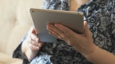 Yaşlı kadın kanepede oturan bir dijital tablet holding