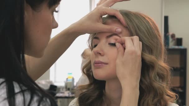 Maquillaje artista pega las pestañas a la chica — Vídeo de stock