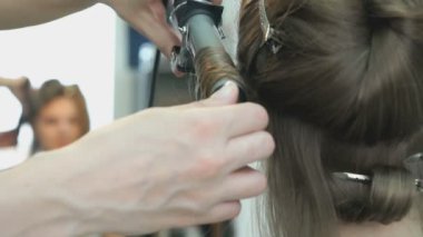Stilist bukleler kahverengi saçlı bir kıvırma kullanarak yapar