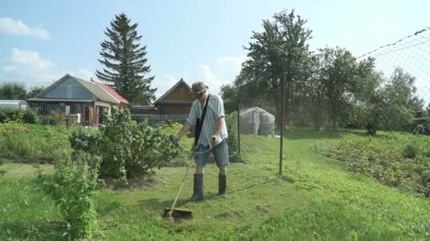 Arbetaren slåtter ett gräs med trimmer utomhus — Stockvideo