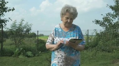 Yaşlı kadın bir dijital tablet açık havada tutan 80s