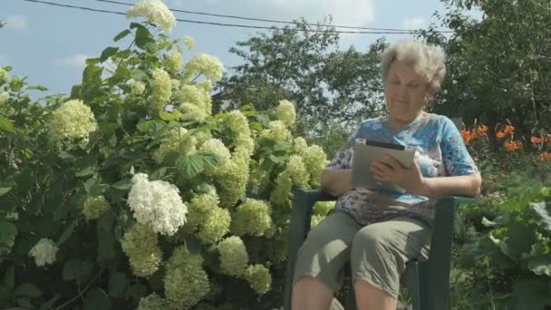 Femme âgée des années 80 tenant une tablette numérique à l'extérieur — Video