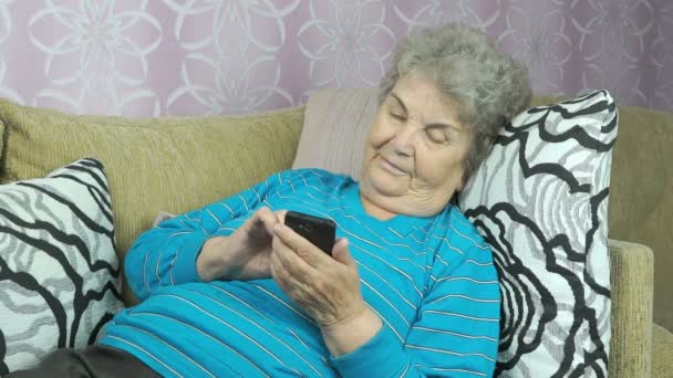 Bejaarde vrouw houdt een mobiele telefoon binnen — Stockvideo