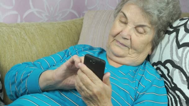 Bejaarde vrouw houdt een mobiele telefoon binnen — Stockvideo