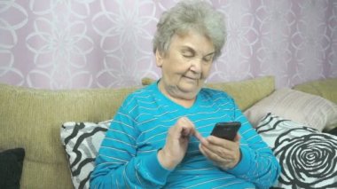 Yaşlı kadın bir cep telefonu kullanarak bej kanepede oturuyor