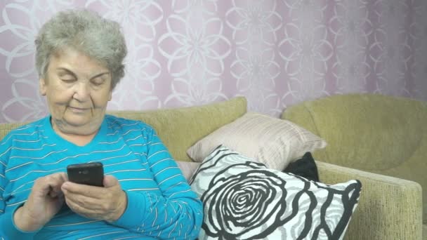 Donna anziana che utilizza un telefono cellulare si siede su un divano — Video Stock