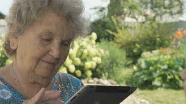 Yaşlı kadın bir dijital tablet açık havada tutan 80s