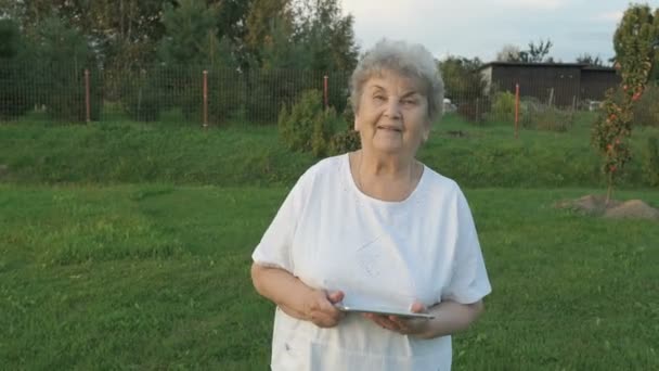 Mujer de 80 años sosteniendo la tableta del ordenador al aire libre — Vídeo de stock