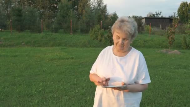 Aged woman 80s holding a digital tablet outdoors — Stock Video